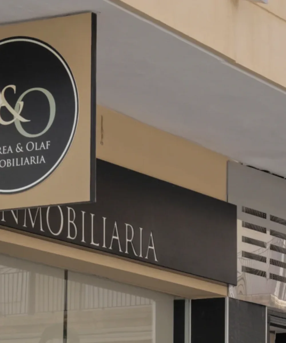Exterior signage of the Andrea & Olaf real estate office, featuring a circular logo and black stone cladding on the storefront facade.