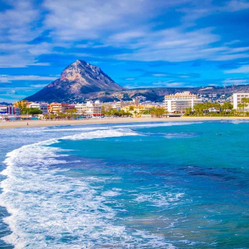 Panoramic view of Jávea beach with Montgó mountain in the background. Residential buildings line the coast.