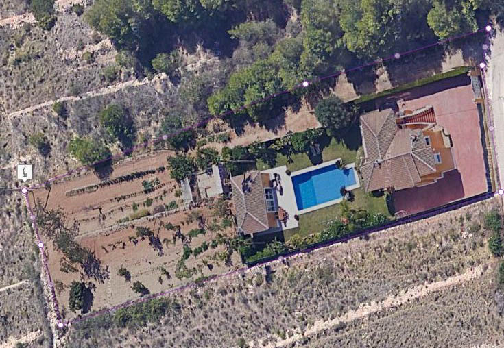 Aerial view of the delimited plot featuring the main villa, a 15x6 m swimming pool, the barbecue building, and a large flat agricultural area.
