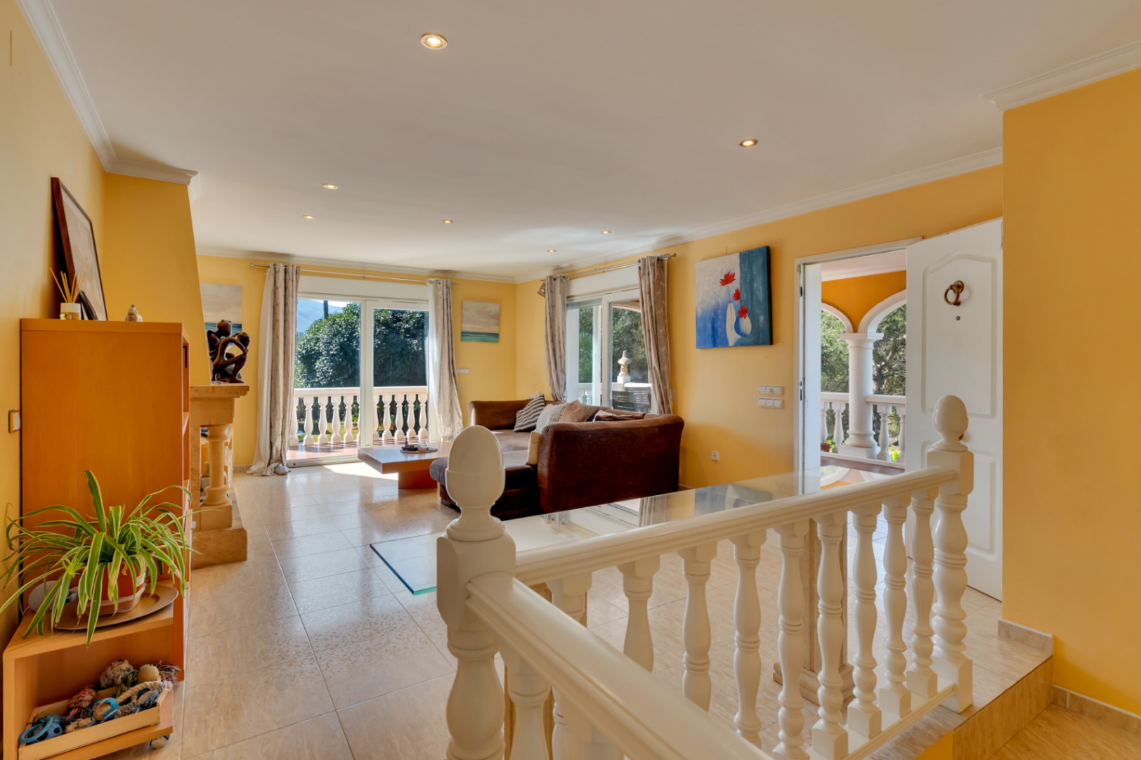 Bright living area featuring tiled flooring, recessed lighting, and sliding glass doors that open onto a terrace with classic stone balustrades and garden views.