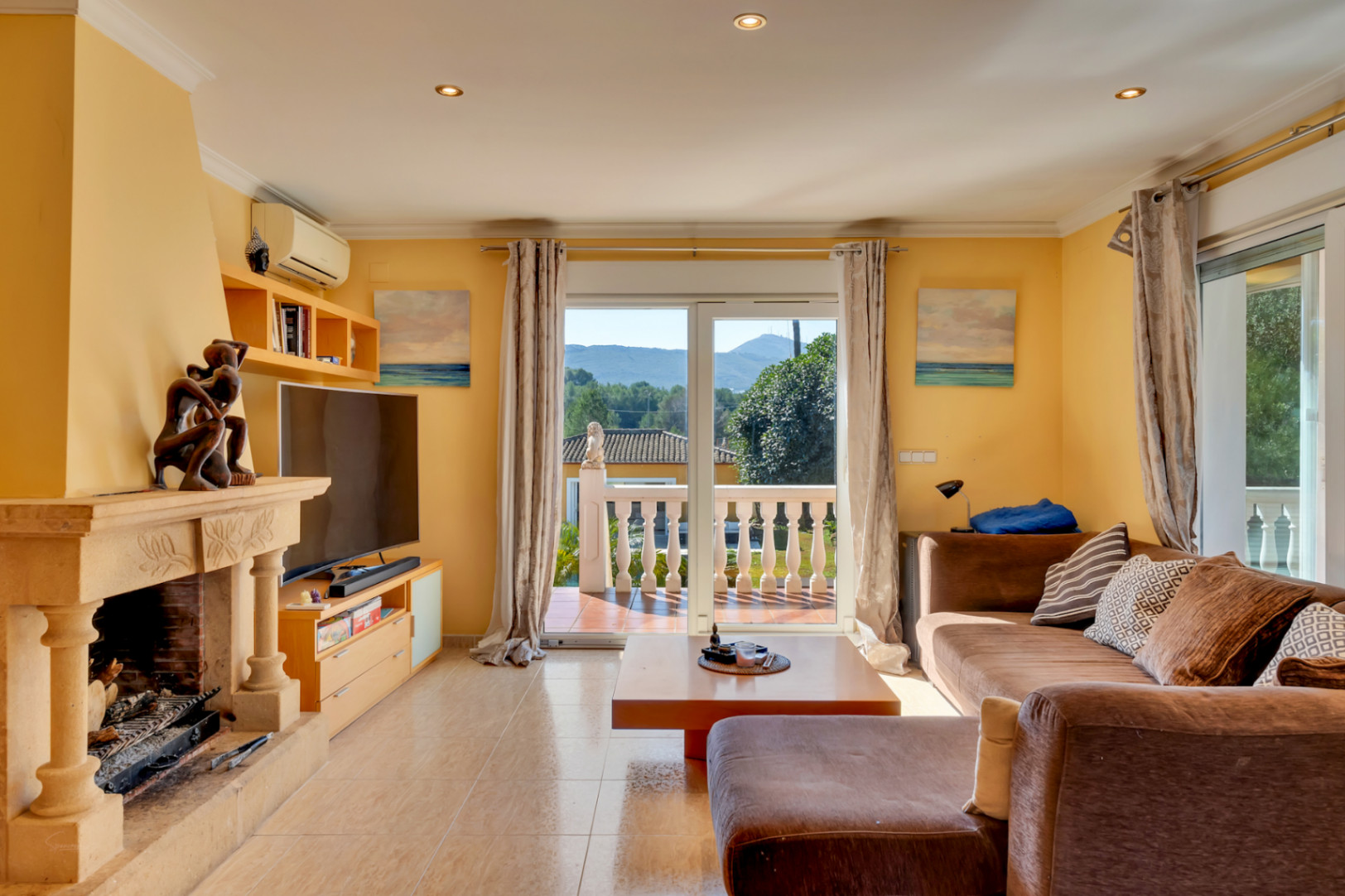 Bright living room featuring a carved stone fireplace, ceramic flooring, and sliding glass doors opening onto a terrace with mountain views.