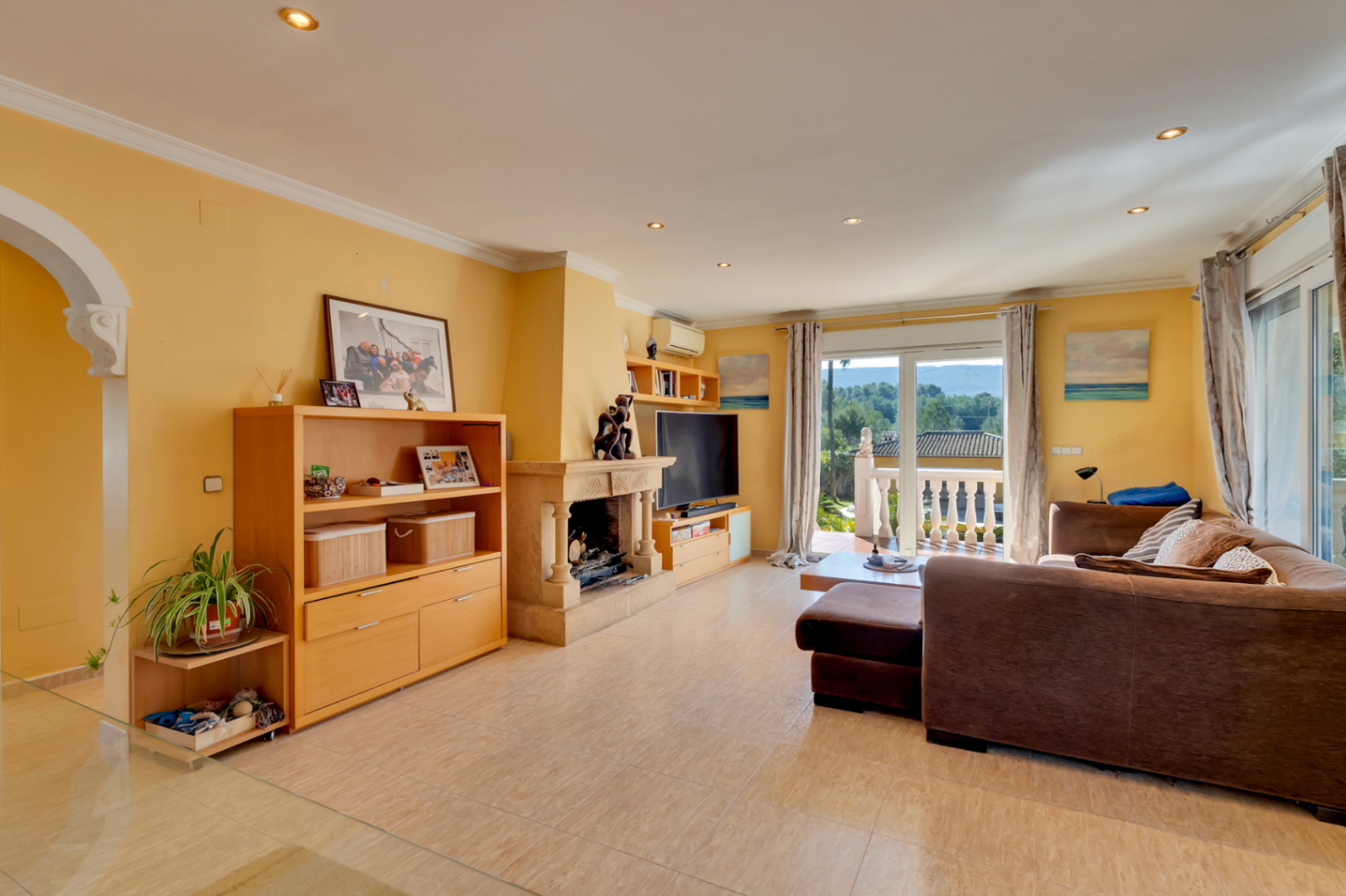 Bright living room featuring a natural stone fireplace, ceramic flooring, and direct access to a terrace with open views of the surrounding greenery.