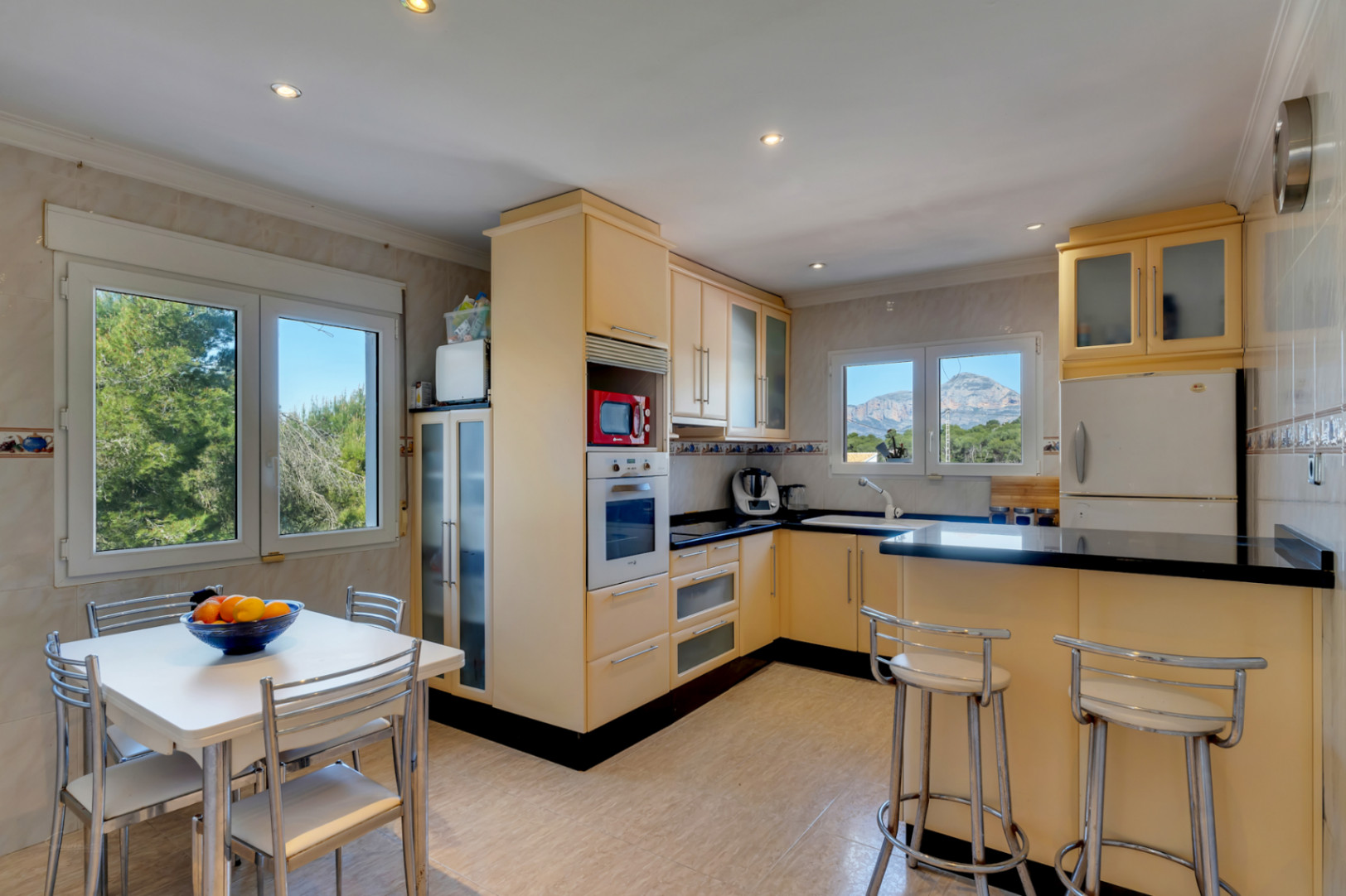 Fully equipped kitchen featuring black granite countertops, a breakfast bar, and an integrated dining area. Large windows offer natural light and views of the Montgó mountain.