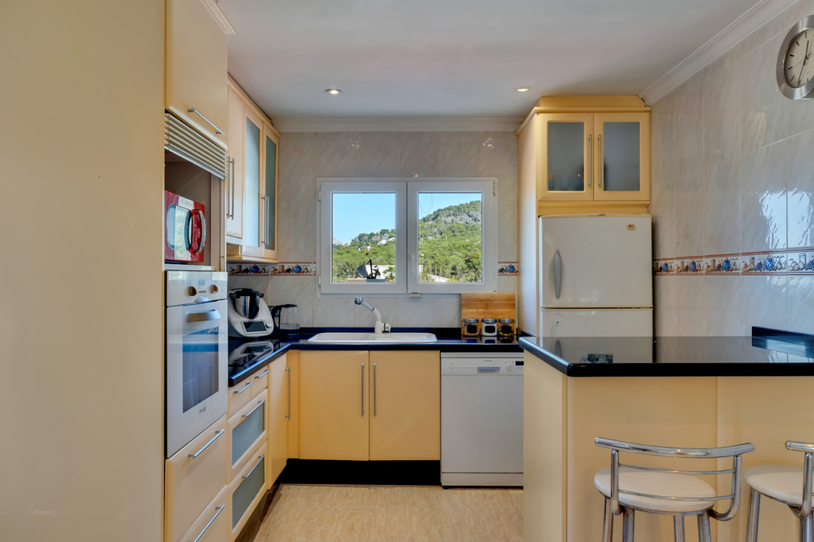 Functional kitchen featuring cream cabinetry, black granite countertops, and a window overlooking the mountains. Equipped with integrated appliances and a breakfast bar.