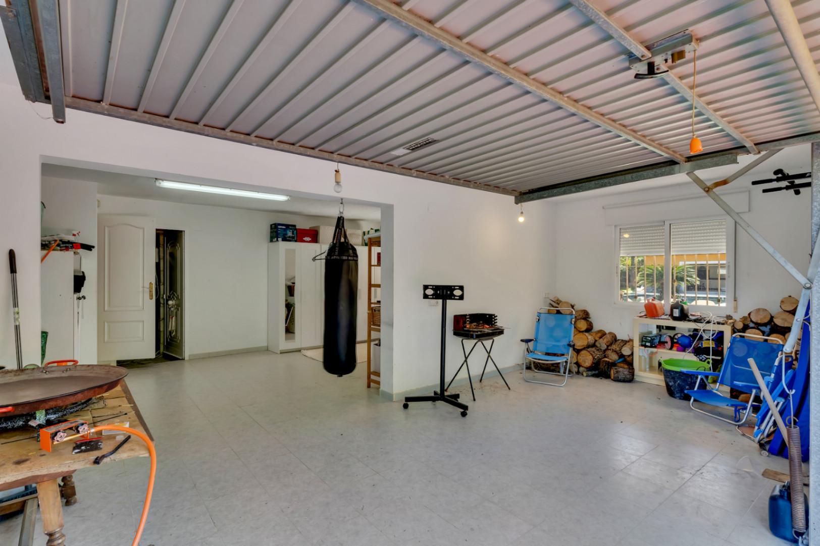 Spacious garage featuring tiled floors and metal roofing, currently used as a storage and fitness area with direct access to the main house.
