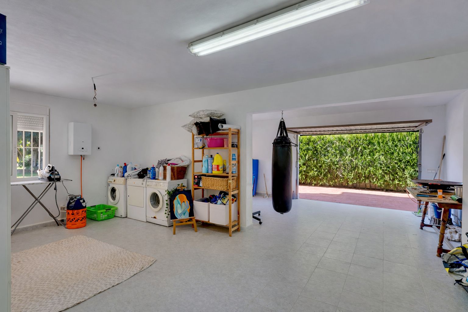 Spacious multipurpose room featuring a laundry area, gym space with a punching bag, and direct access to the driveway through a large garage door.