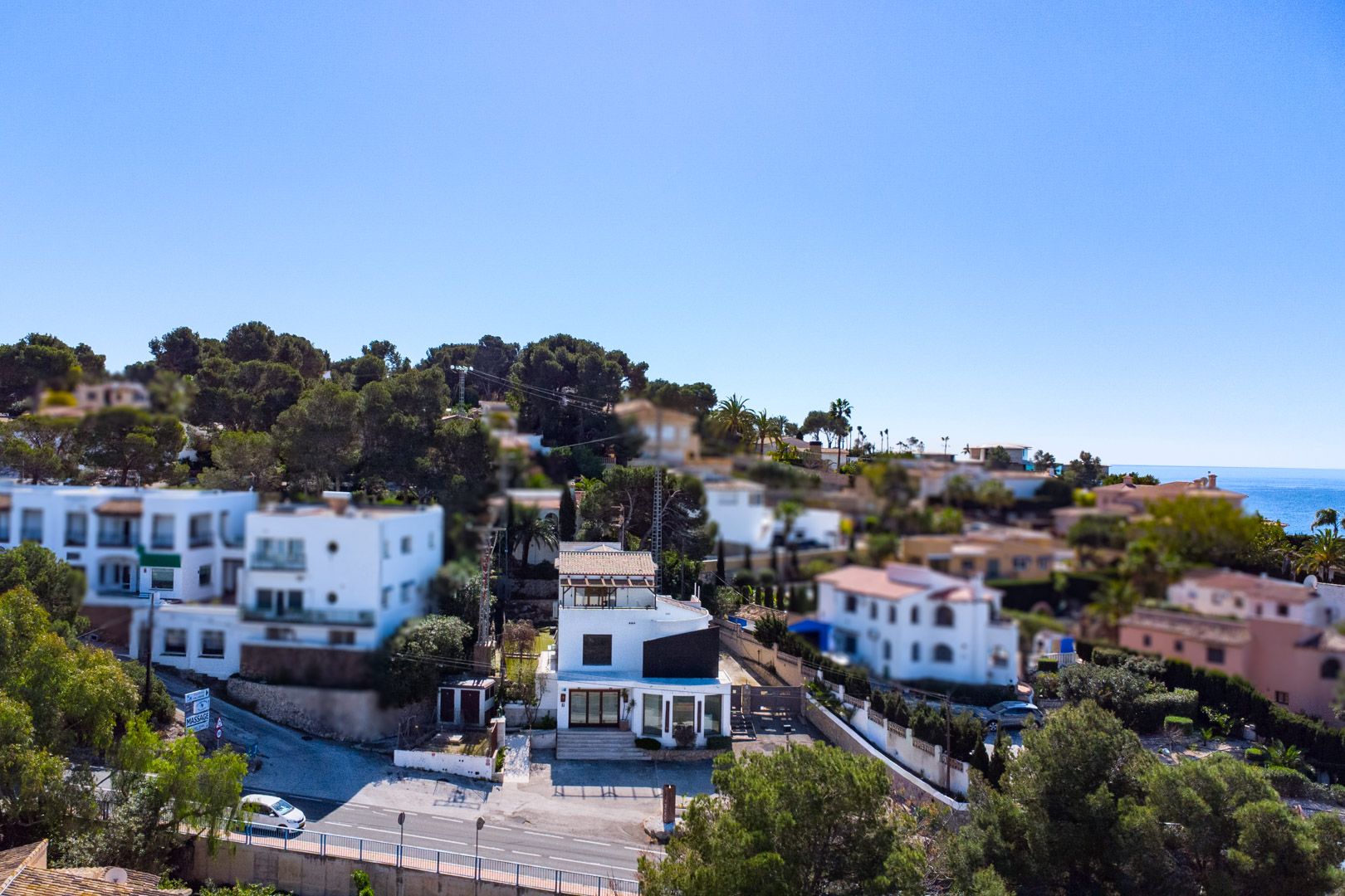 Aerial view of the property along the Moraira-Calpe road, featuring a white facade, large commercial windows, and views of the Mediterranean Sea.
