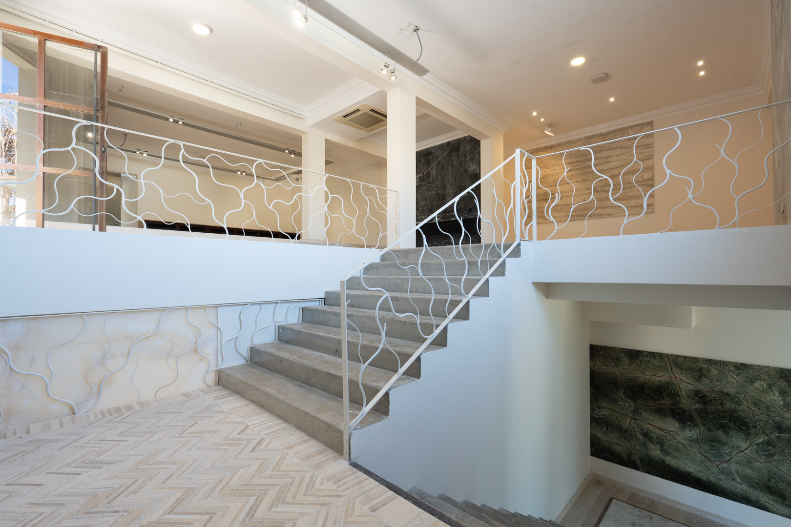 Architectural staircase featuring an organic-patterned white railing, connecting open-plan commercial levels with herringbone flooring and decorative stone wall panels.