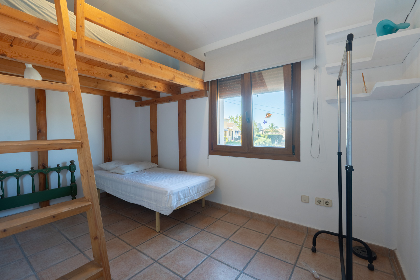 Bedroom featuring a solid wood bunk bed structure, rustic tiled flooring, and a wooden-framed window providing natural light.