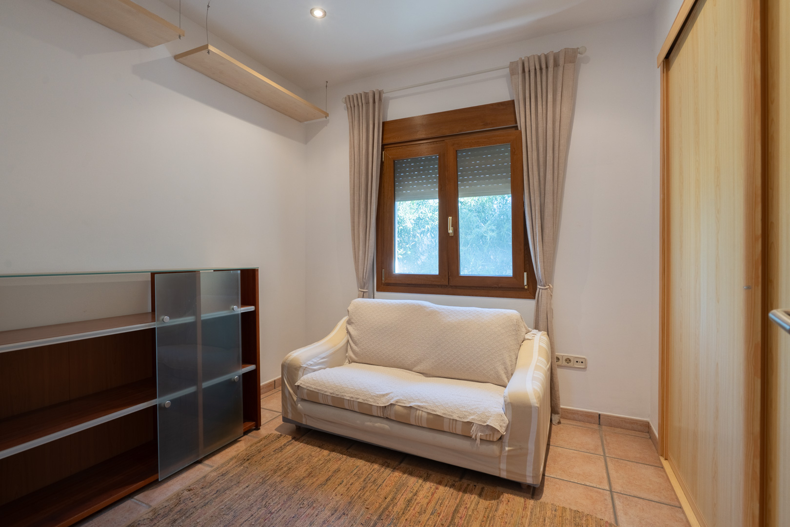 Bedroom featuring terracotta-style flooring, a light wood built-in wardrobe, and a wooden window frame with integrated shutters.