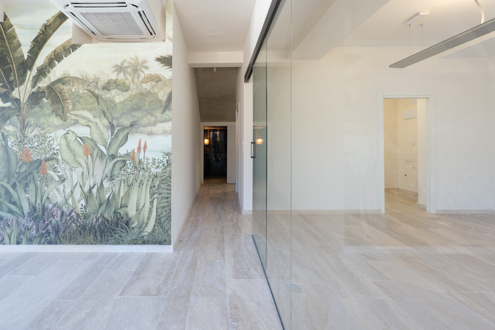 Bright commercial interior featuring light stone-effect flooring, a large glass partition, and a tropical mural. Equipped with a ceiling-mounted AC unit.