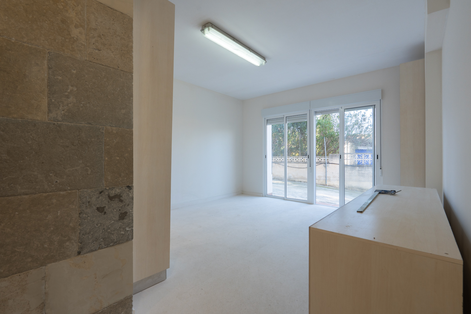 Bright commercial space featuring a natural stone accent wall, fluorescent lighting, and large sliding glass doors providing direct access to the exterior.