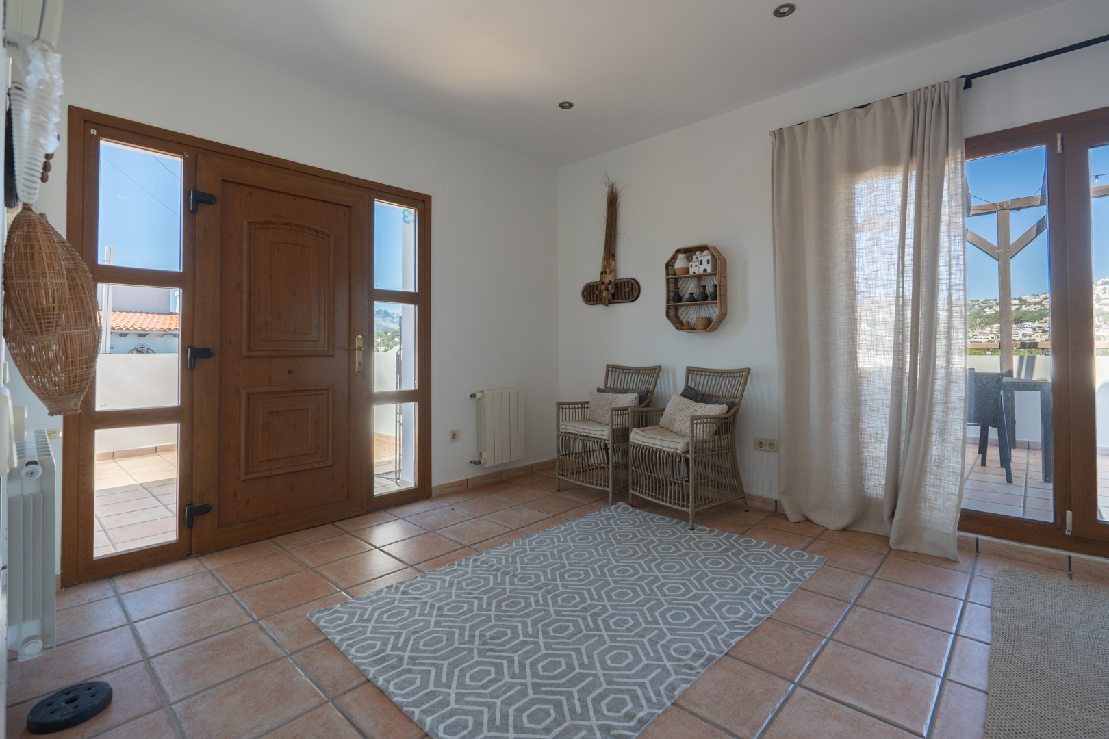 Bright entrance hall featuring terracotta floor tiles, a wooden front door with side panels, and access to a terrace with a wooden pergola.