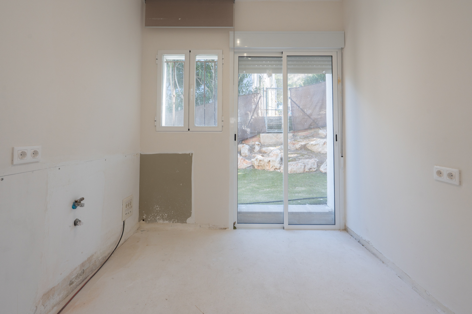 Bright room featuring plumbing pre-installation, white walls, and a sliding glass door providing direct access to the outdoor garden area.