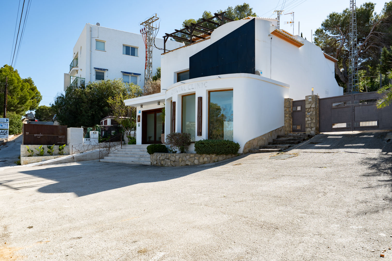 Contemporary exterior featuring a white curved facade, large display windows, a paved parking area, and a secure gated entrance with stone accents.