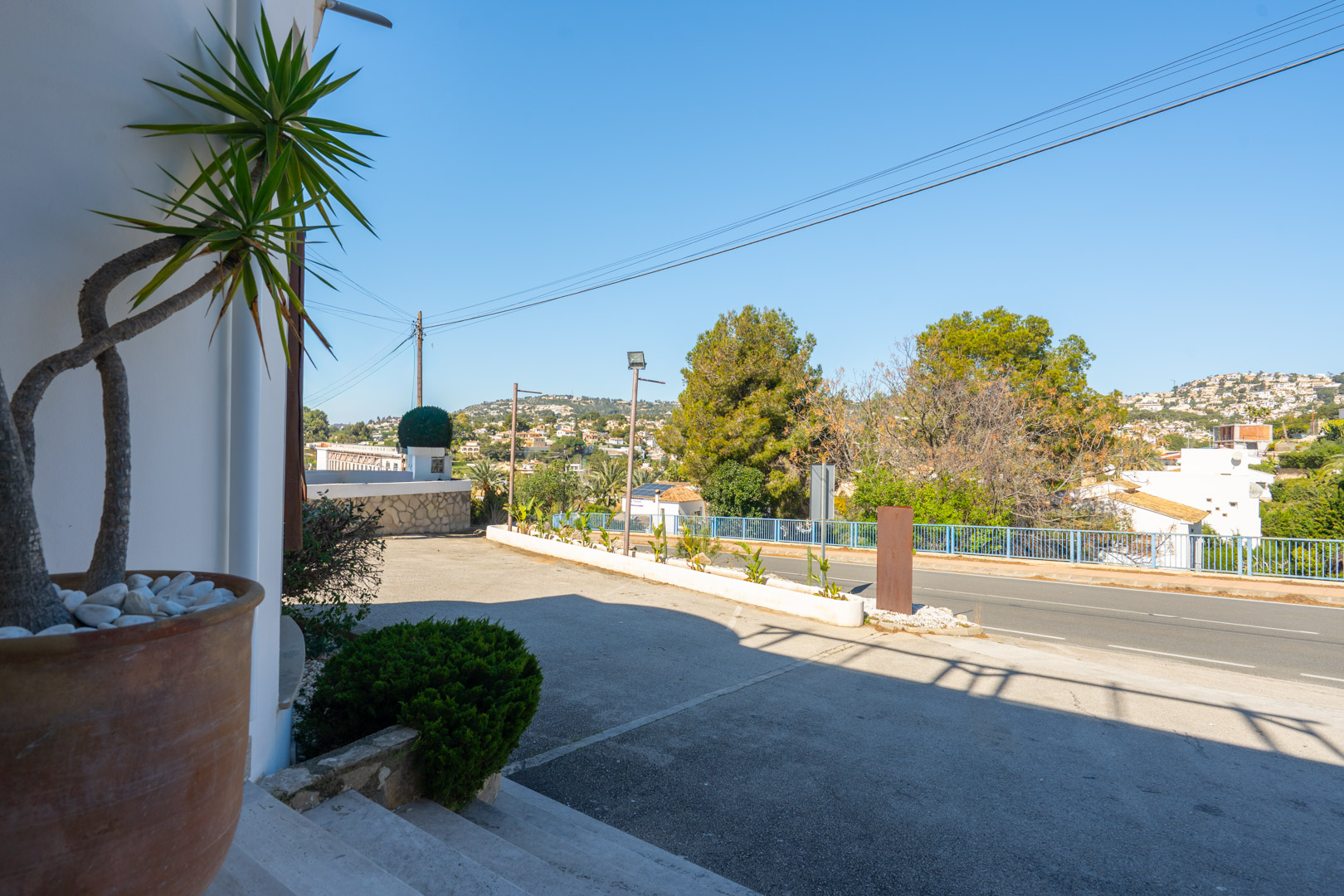 Exterior parking area and main entrance featuring high visibility from the road, with Mediterranean landscaping and open views of the surrounding hills.