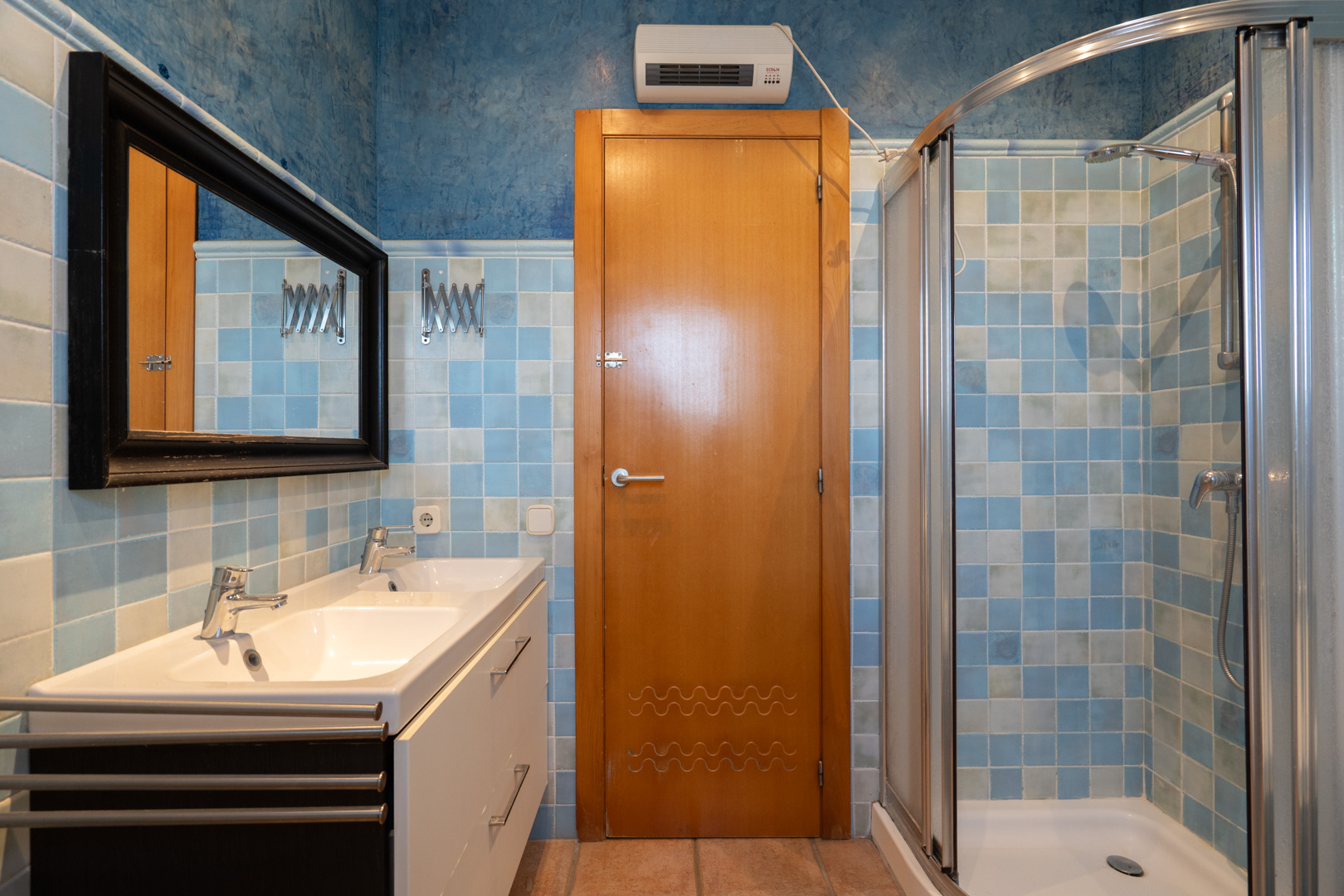 Functional bathroom featuring a double vanity, curved glass corner shower, and walls finished with blue mosaic tiles and textured blue paint.