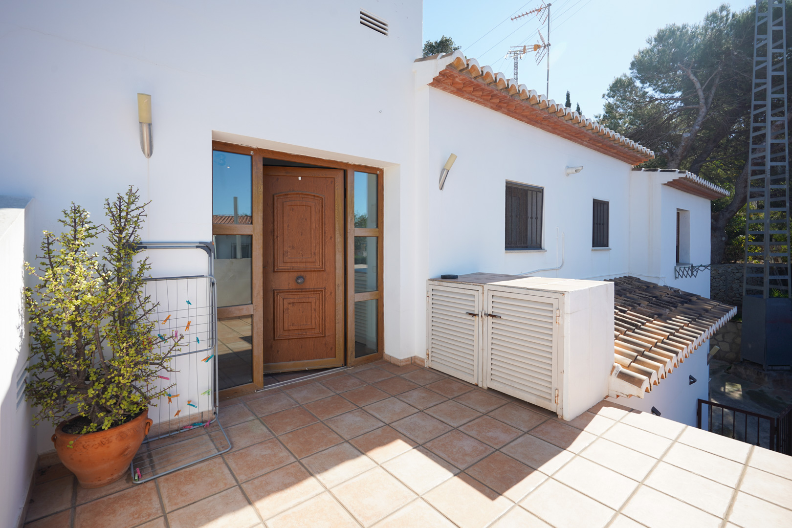 Independent access to the upper residence featuring a carved wooden door, rustic tiled terrace, and built-in outdoor storage units on a white facade.
