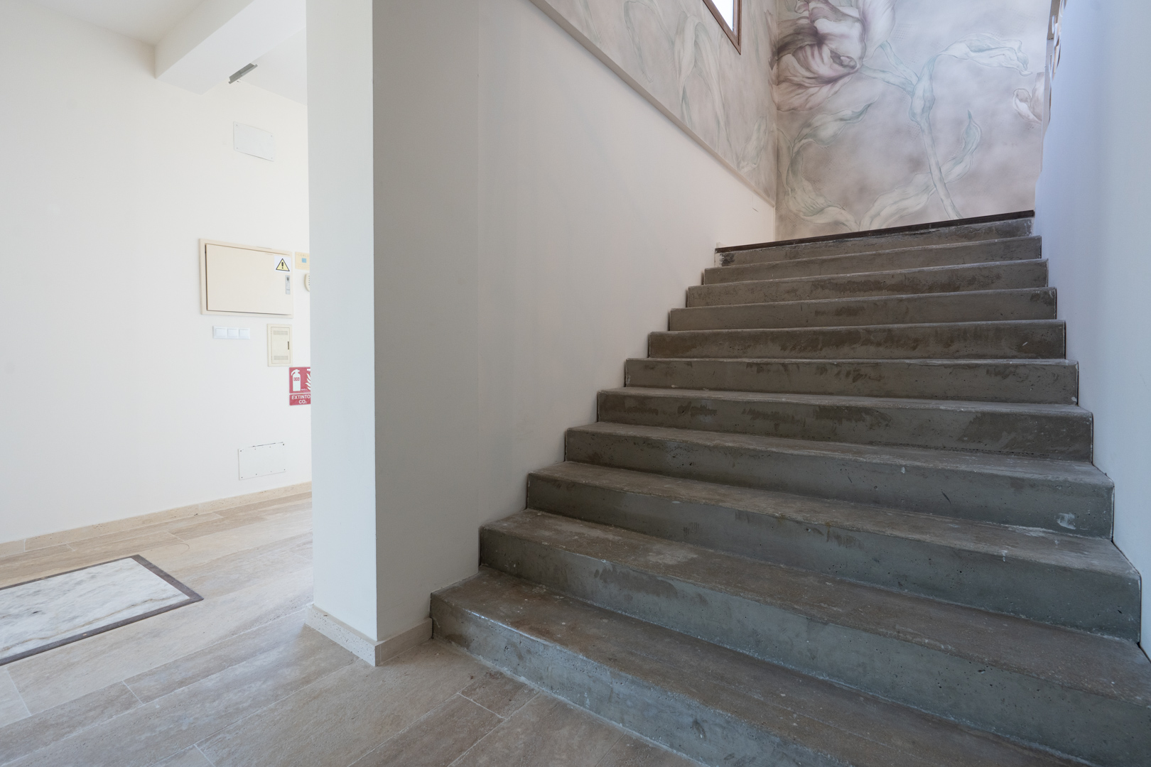 Interior concrete staircase featuring a decorative floral mural on the adjacent wall and neutral stone-effect floor tiling throughout the hallway.