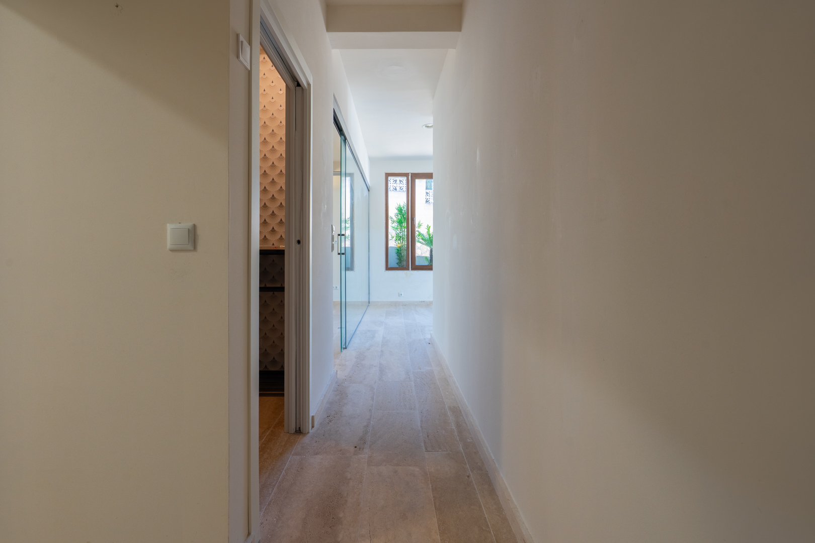 Interior hallway featuring natural stone flooring, white walls, and access to rooms with glass partitions and decorative textured wallpaper.