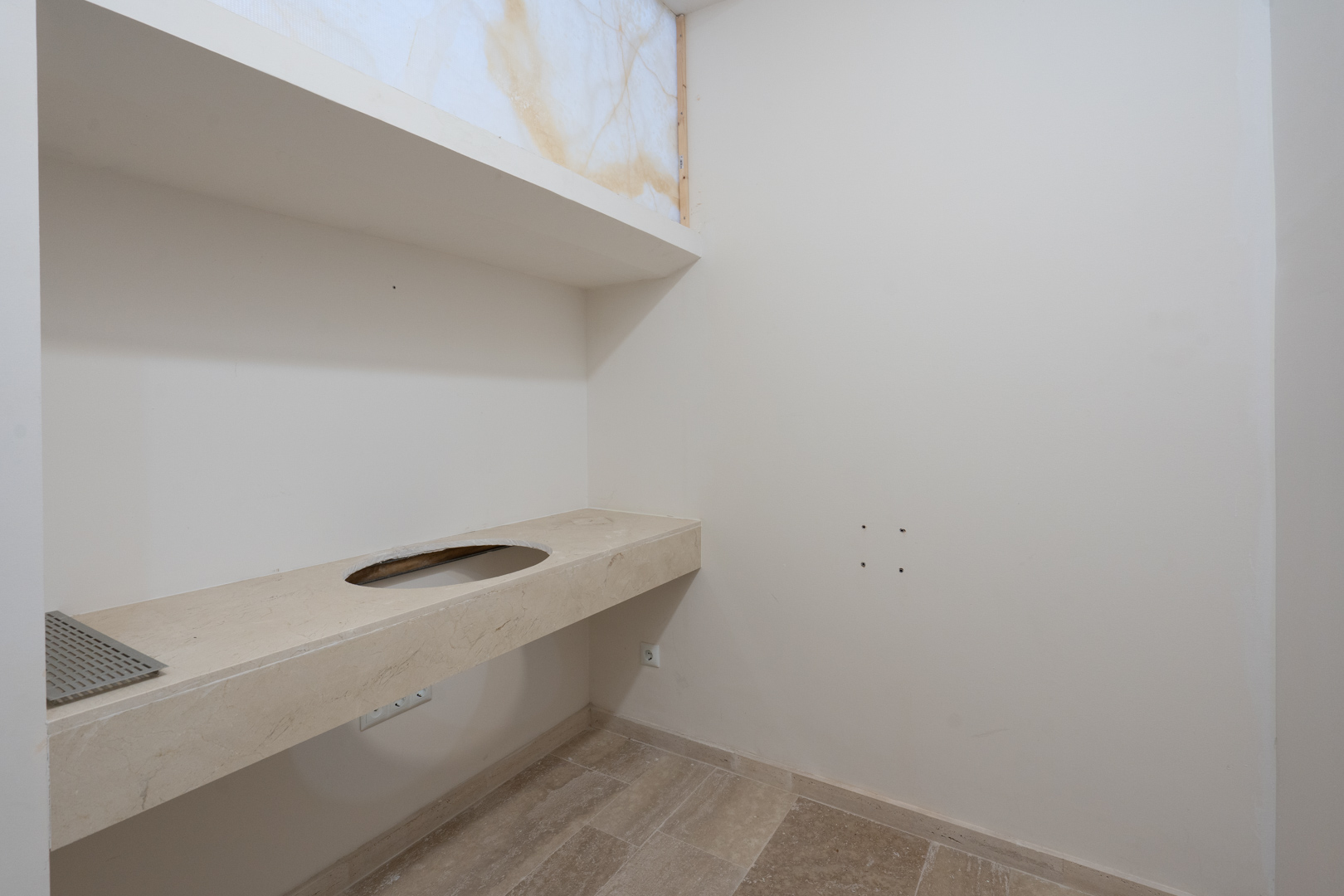 Natural stone vanity top with integrated sink cutout, matching upper shelving, and neutral-toned tiled flooring in a minimalist space.