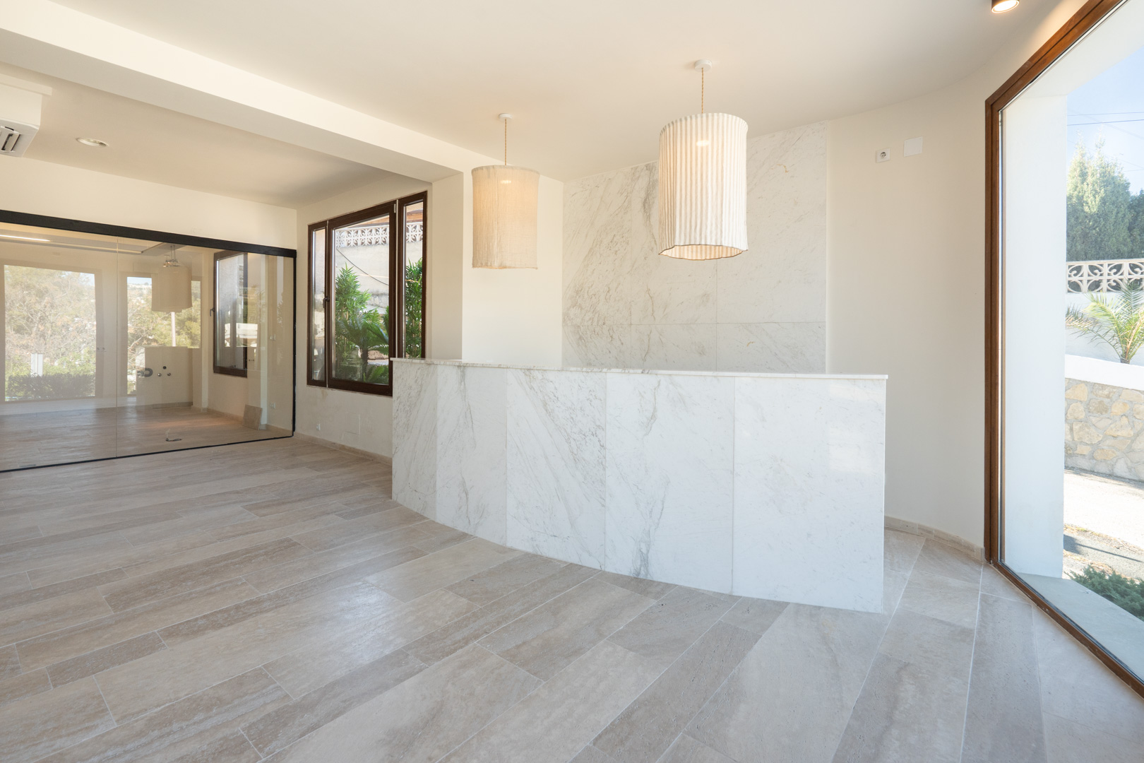 Professional reception area featuring a white marble counter, matching wall accents, fabric pendant lights, and large glass partitions.