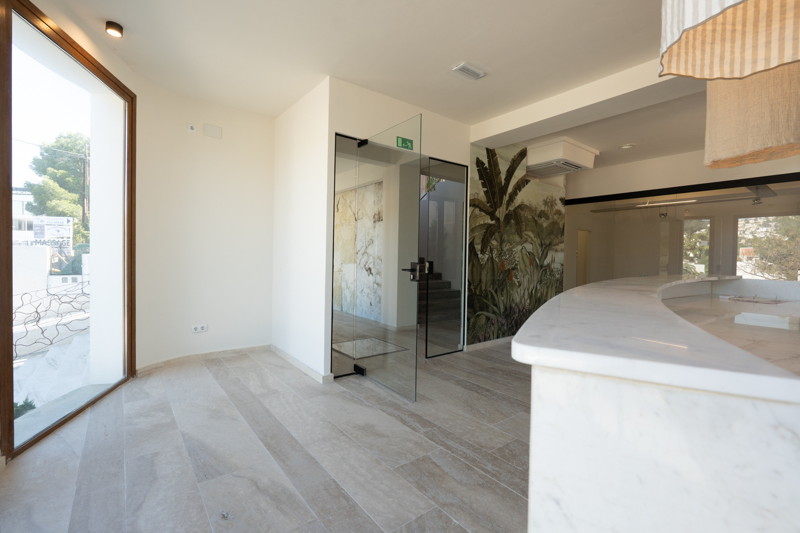 Reception area featuring a curved white marble counter, stone flooring, and glass doors leading to the internal rooms and staircase.