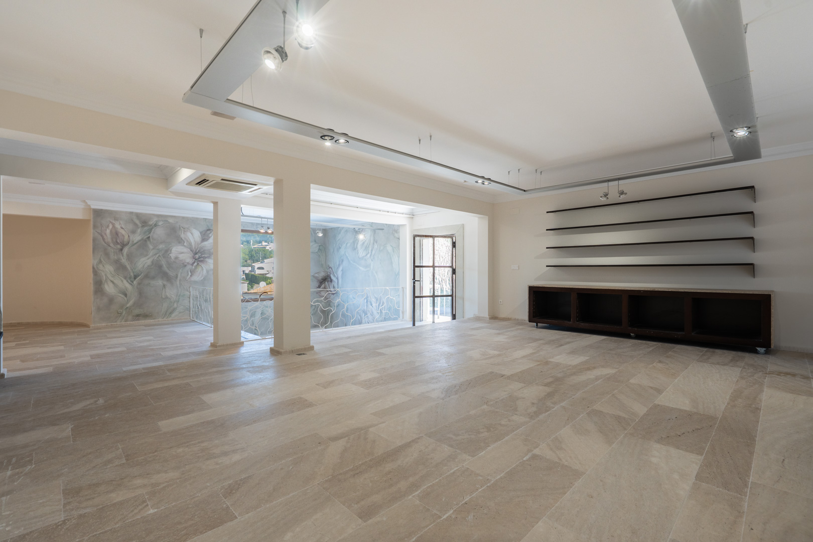 Spacious first-floor commercial area featuring natural stone flooring, track lighting systems, and access to a terrace. Includes decorative wall murals and an ornamental railing.