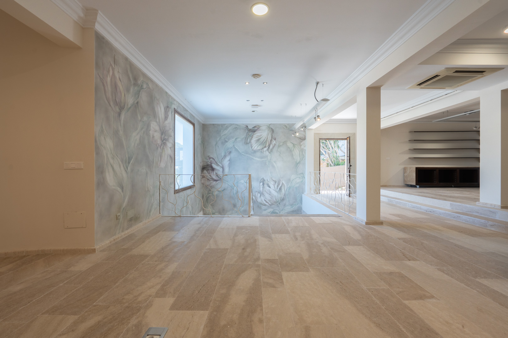 Spacious open-plan area featuring natural stone flooring, decorative floral wall murals, and a custom wrought iron staircase railing.