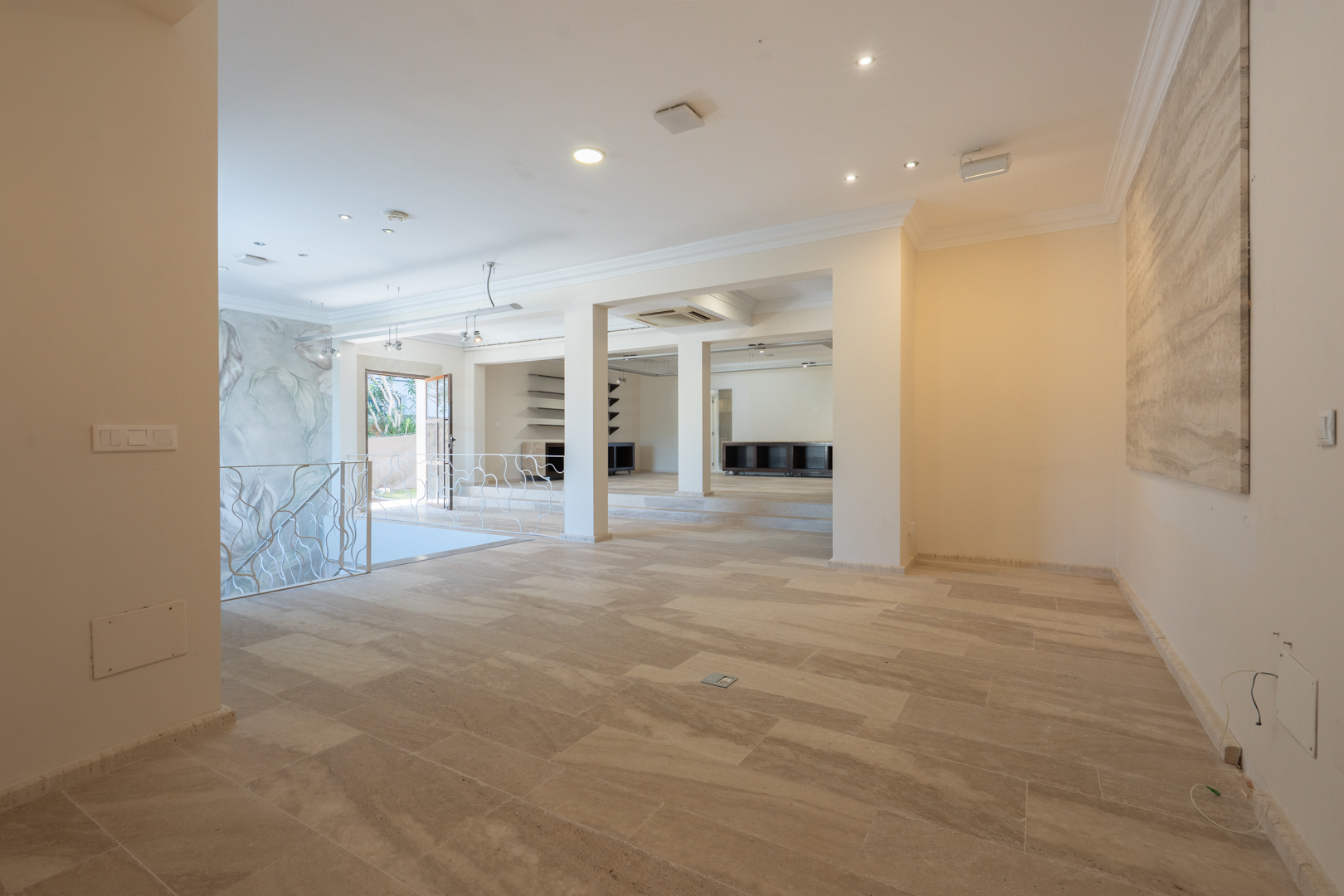 Spacious open-plan first floor featuring natural stone flooring, recessed ceiling lights, and a decorative white wrought-iron staircase railing.