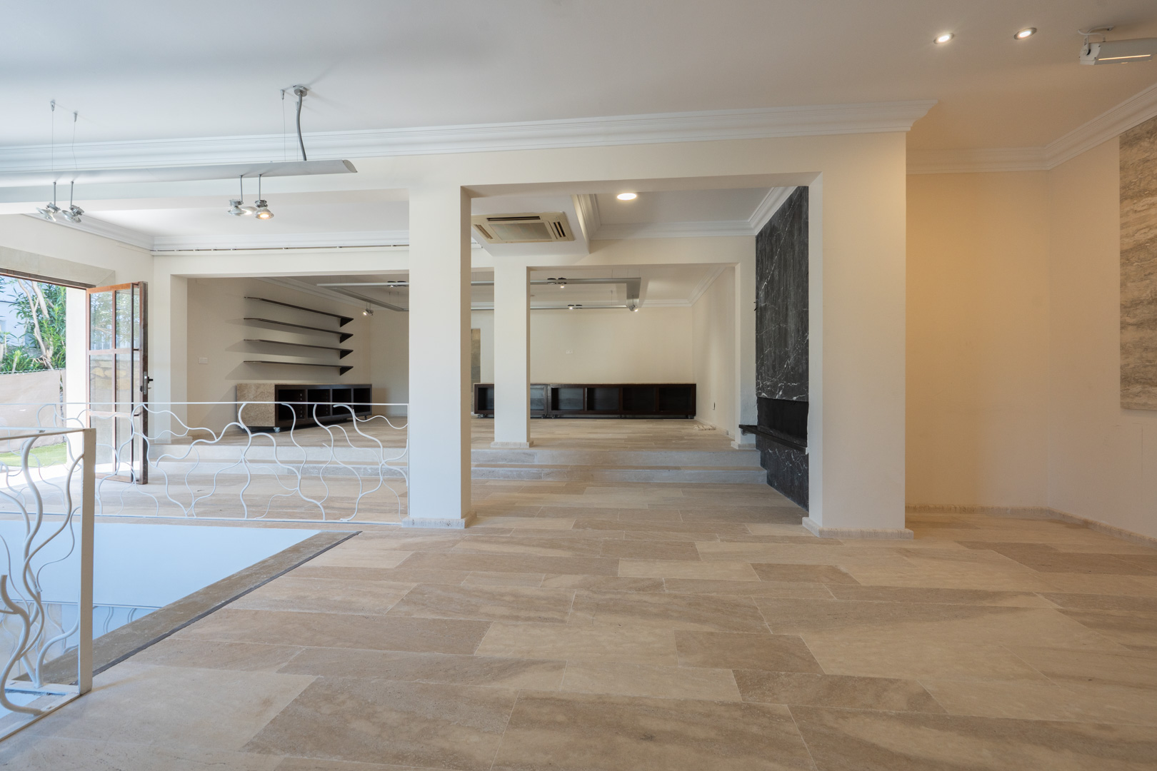 Spacious open-plan interior featuring natural stone flooring, split-level layout, and a black marble accent wall. Equipped with recessed lighting and decorative ironwork.