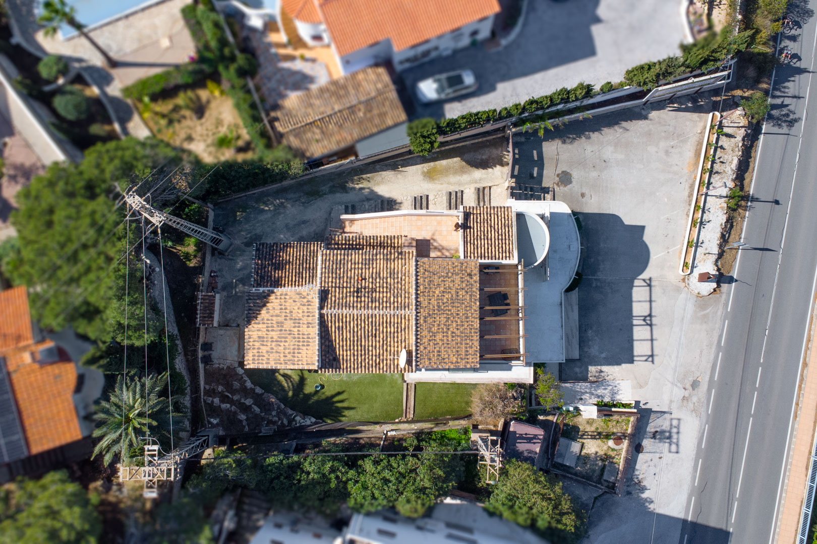 Top-down aerial view showing the property's layout, terracotta tiled roofs, outdoor terraces, and the spacious private parking area adjacent to the main road.