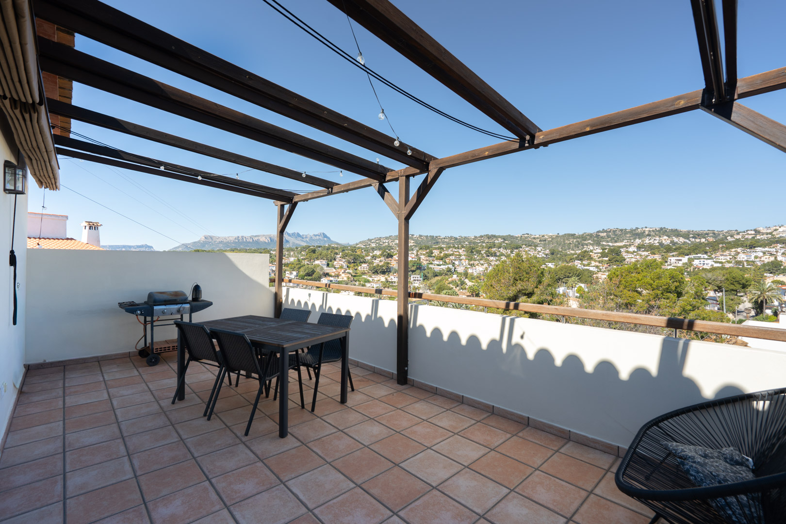 Upper terrace featuring terracotta tiles, a wooden pergola, and a dining area. It offers panoramic views of the Sierra de Bernia mountains and the surrounding valley.