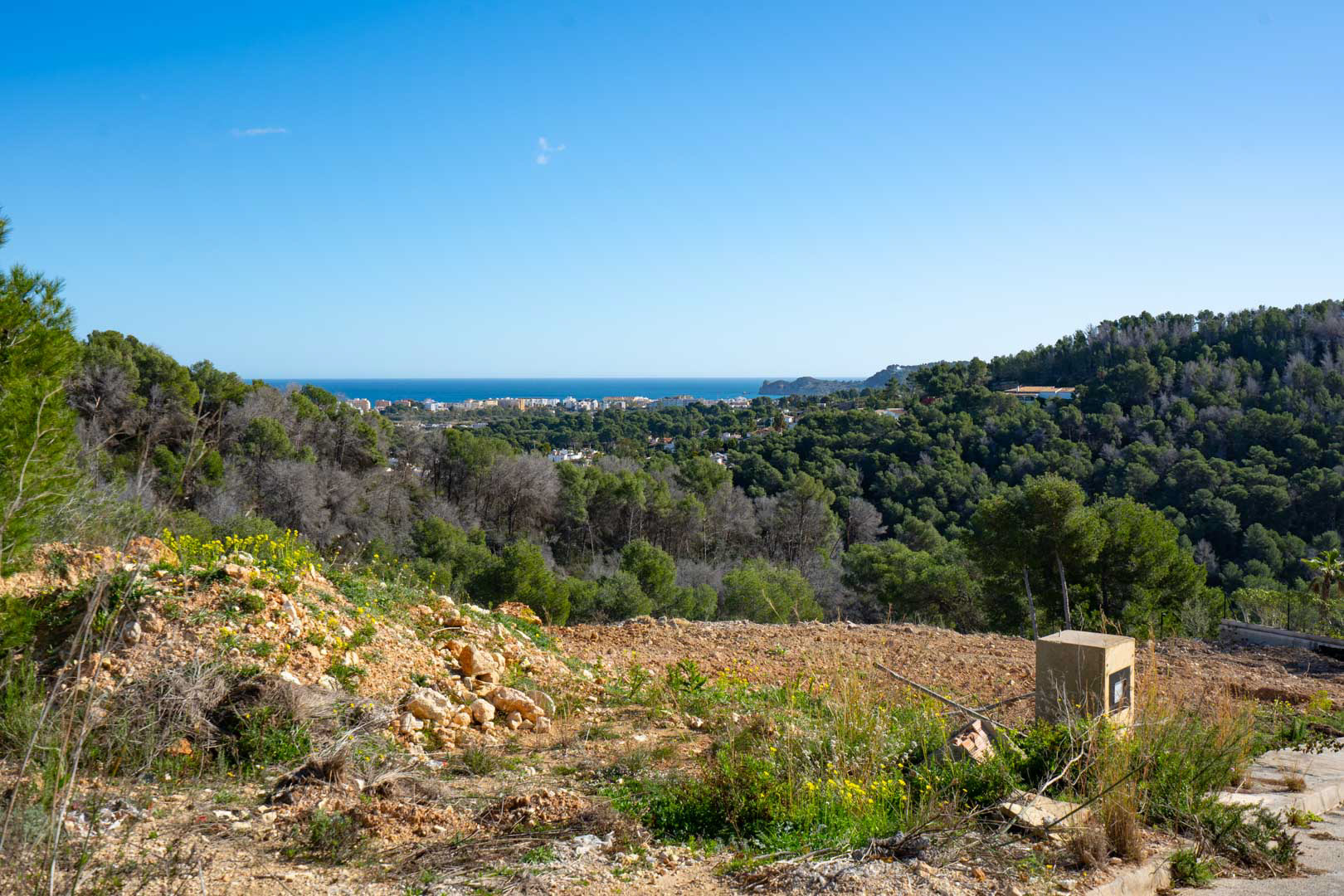 Panoramic sea and coastal views from the elevated plot, surrounded by a lush Mediterranean pine forest and natural landscape under a clear blue sky.