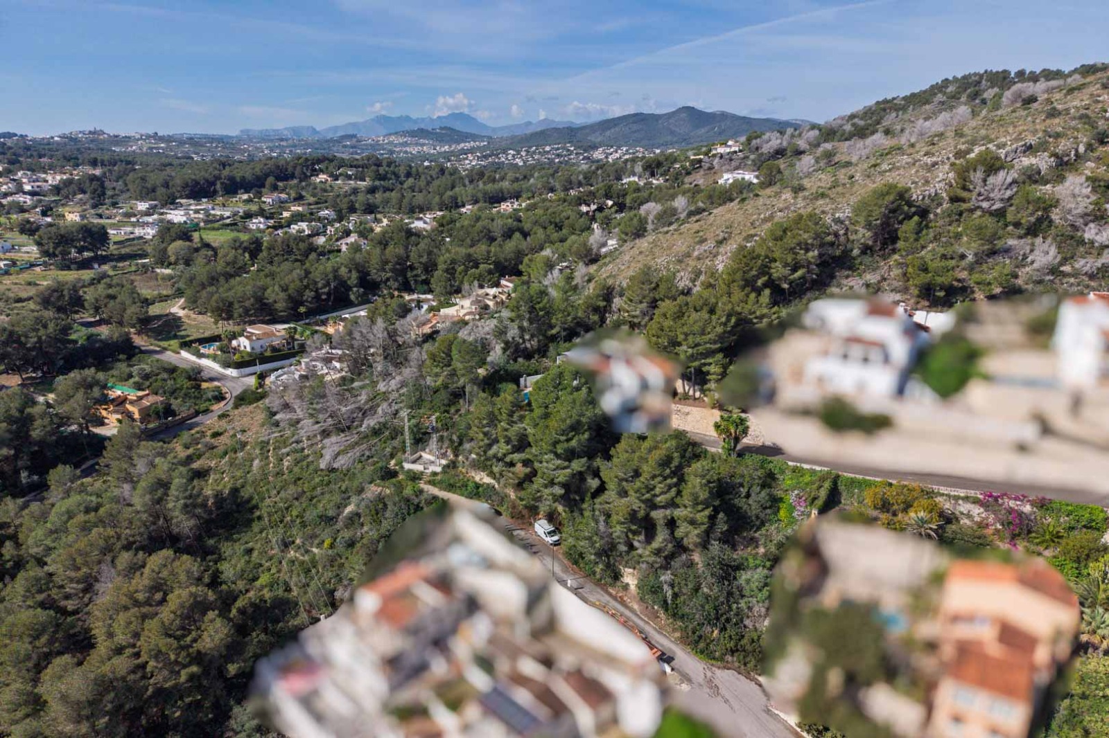 Aerial view of the Sol de Este urbanization, showcasing the dense pine forest, surrounding hills, and distant mountain ranges under a clear blue sky.