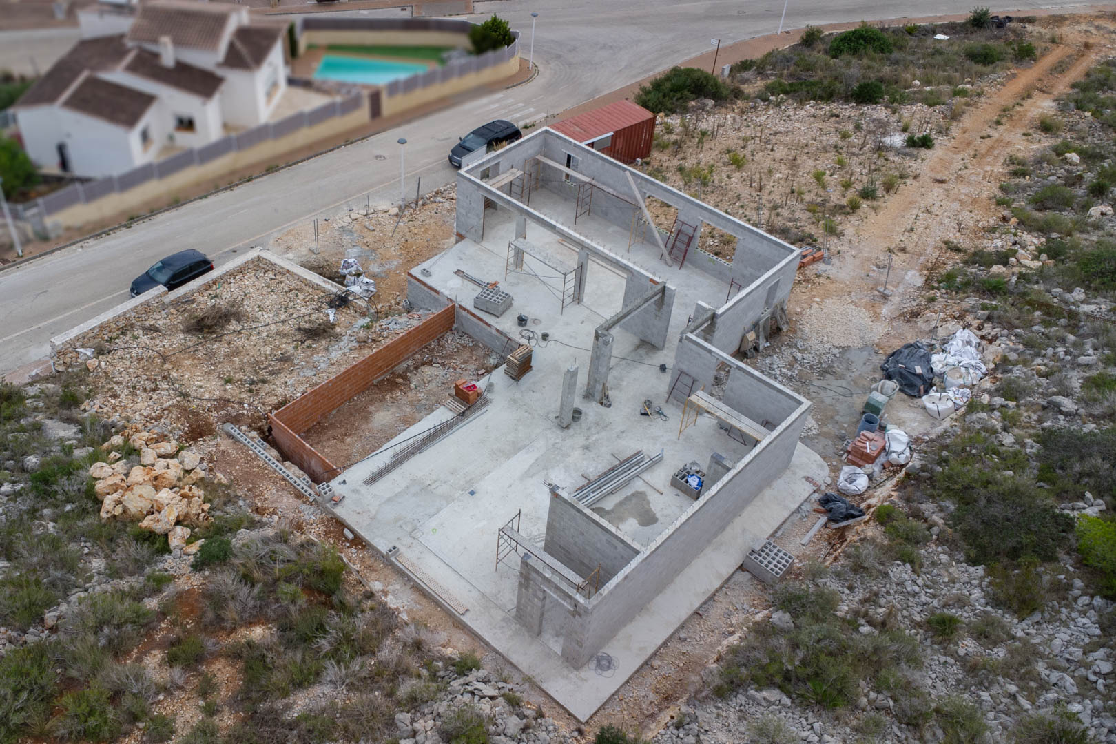 Aerial view of the concrete foundation and block wall structure of the villa under construction, featuring on-site materials and scaffolding.