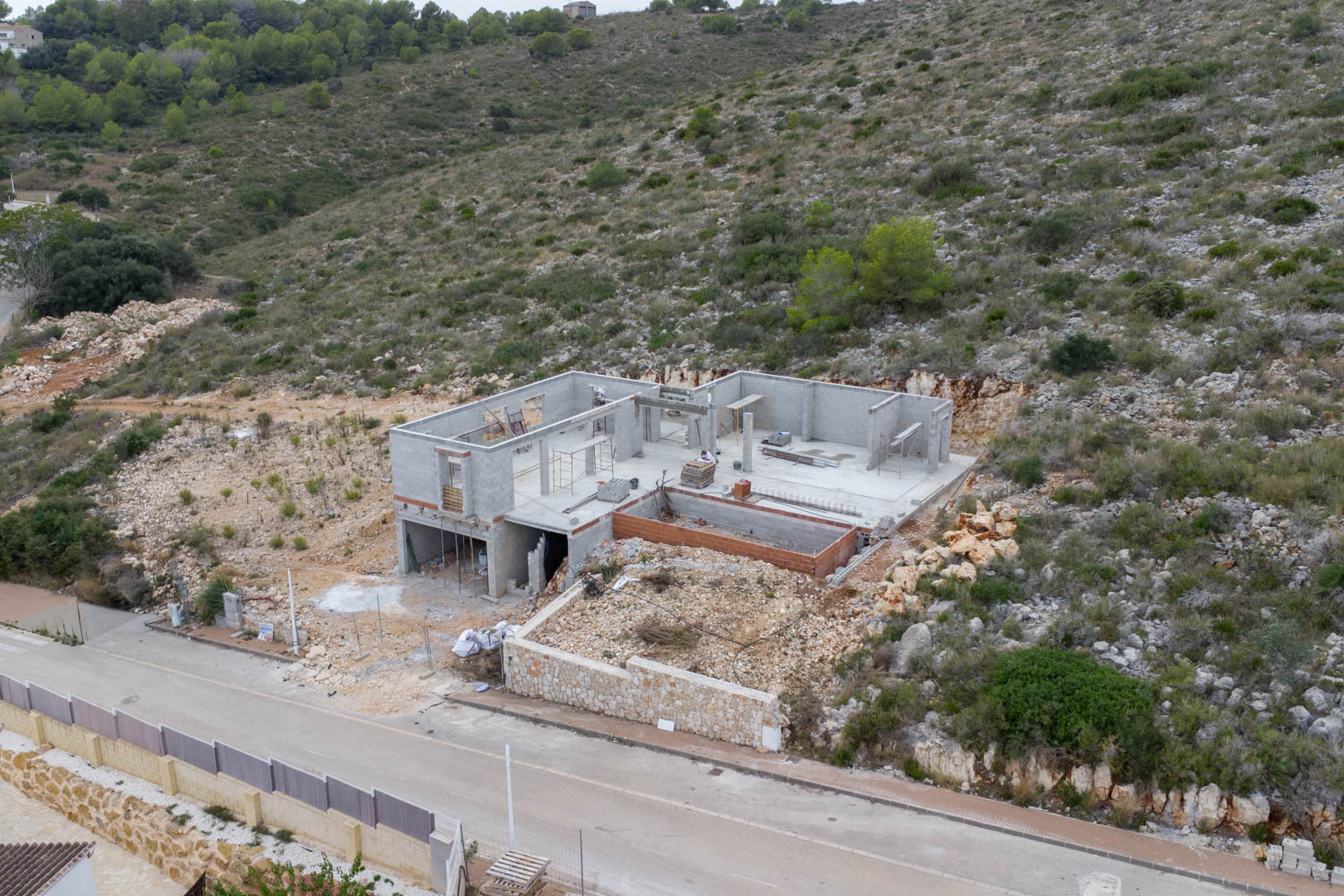 Aerial view of the villa's construction progress in Pedreguer, featuring the concrete block shell and foundation integrated into the natural hillside.