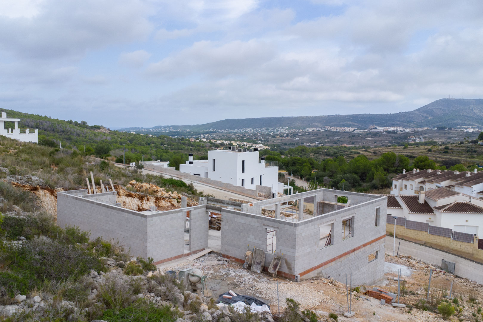 Construction phase of a modern villa in Pedreguer, showing the concrete block structure and panoramic views of the valley and surrounding mountains.