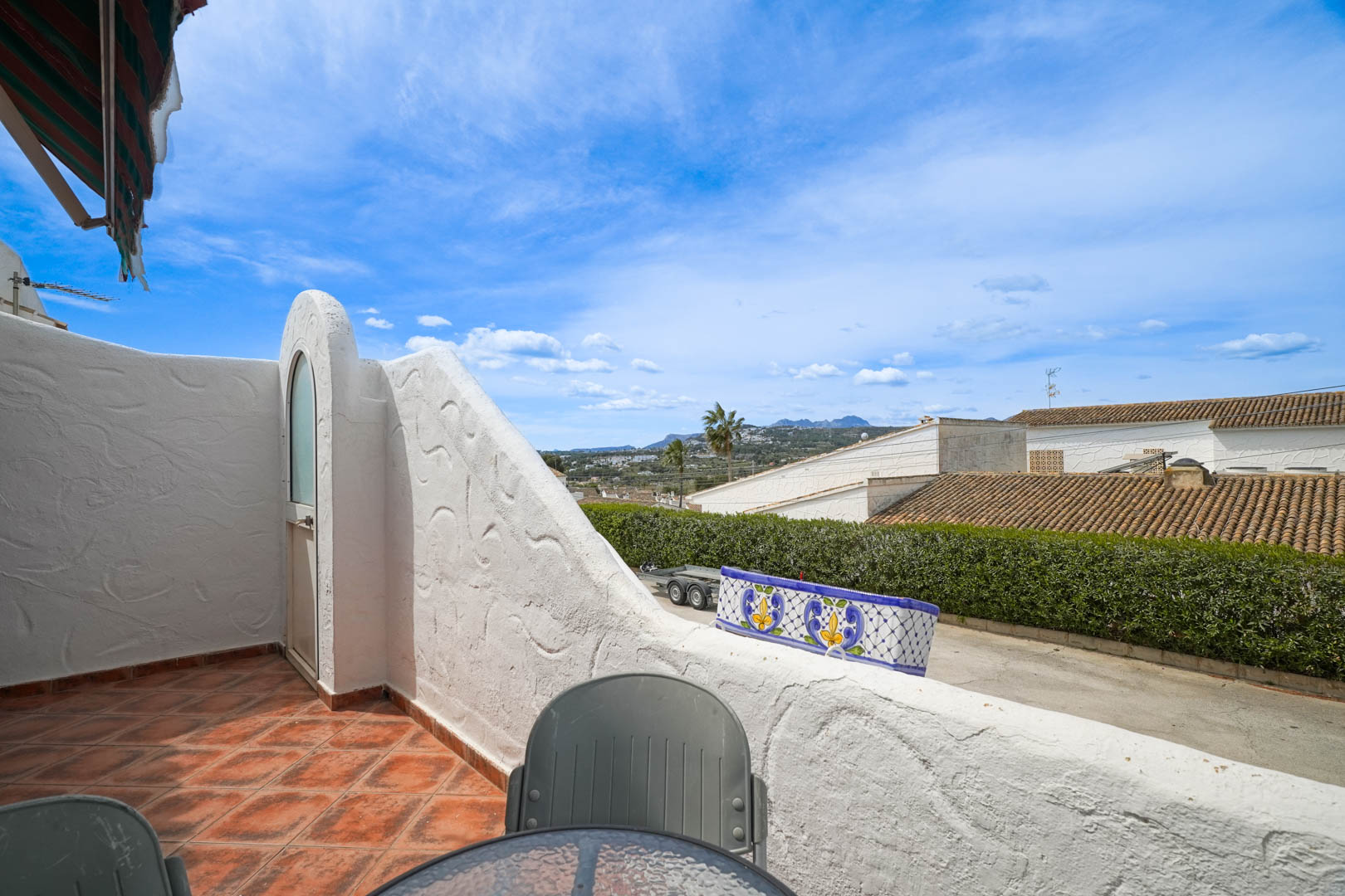 Elevated terrace featuring rustic ceramic tiling and open valley views. The space includes a built-in exterior storage closet and white textured masonry walls.