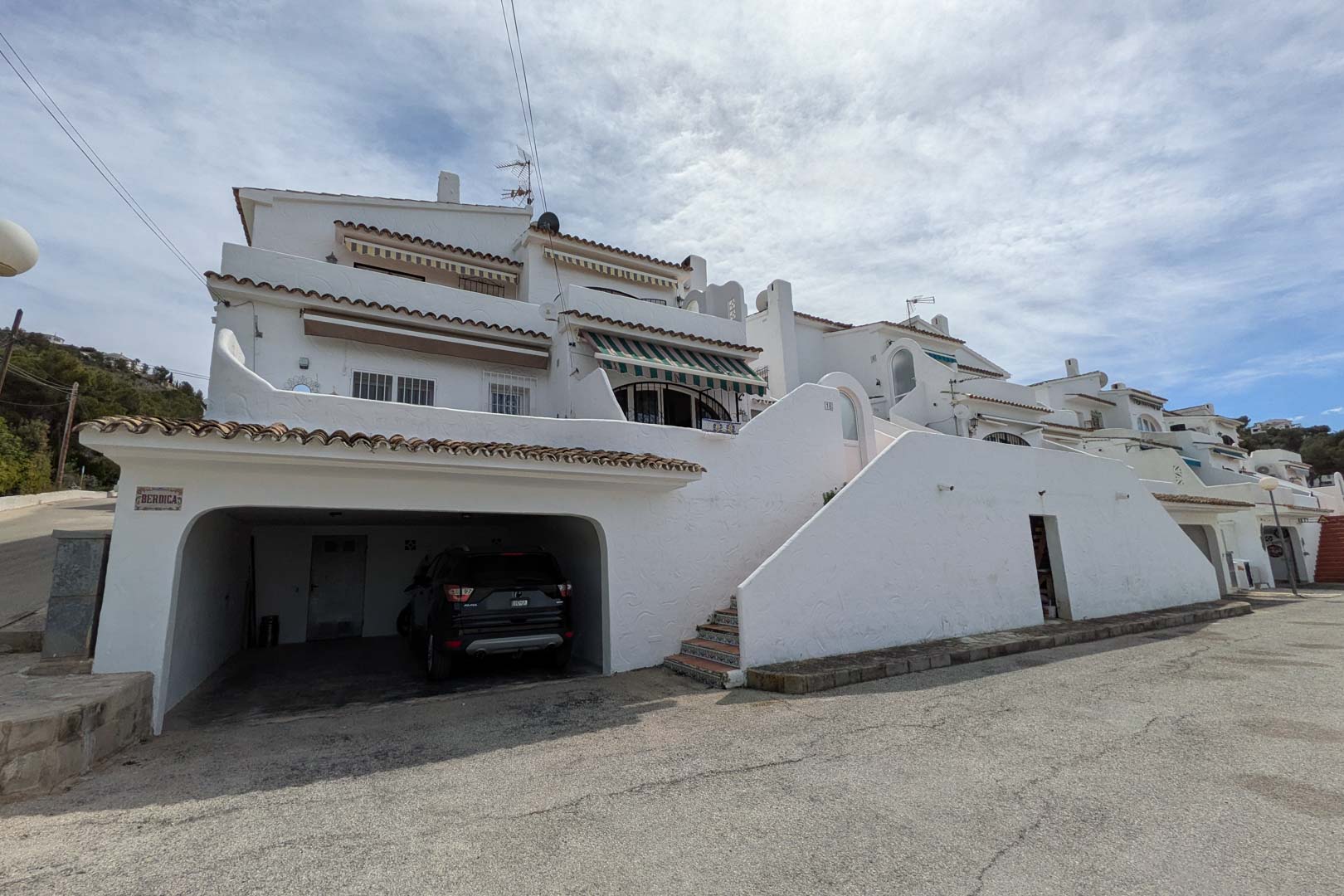 Exterior facade featuring a street-level private garage and tiled stairs leading to the upper residential levels of the Mediterranean building.