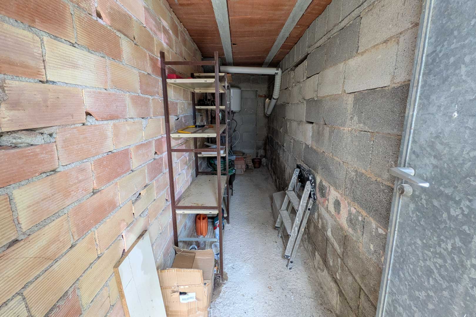 Independent storage room featuring exposed brick and concrete block walls, metal shelving, and a water heater at the rear.