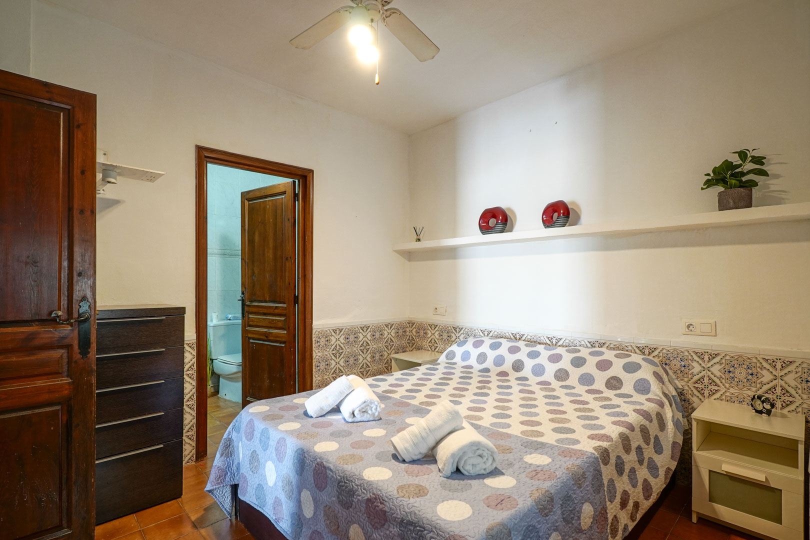 Master bedroom suite featuring decorative tiled wainscoting, a ceiling fan, and direct access to the en-suite bathroom through a classic wooden door.