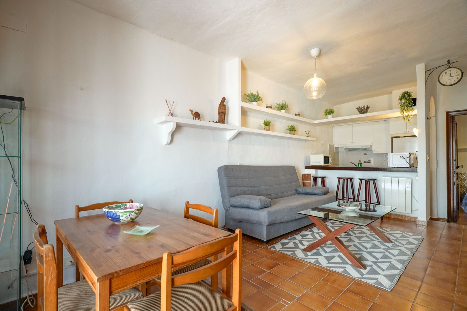 Open-plan living and dining area featuring terracotta tile flooring, built-in plaster shelving, and a semi-integrated kitchen with a breakfast bar.