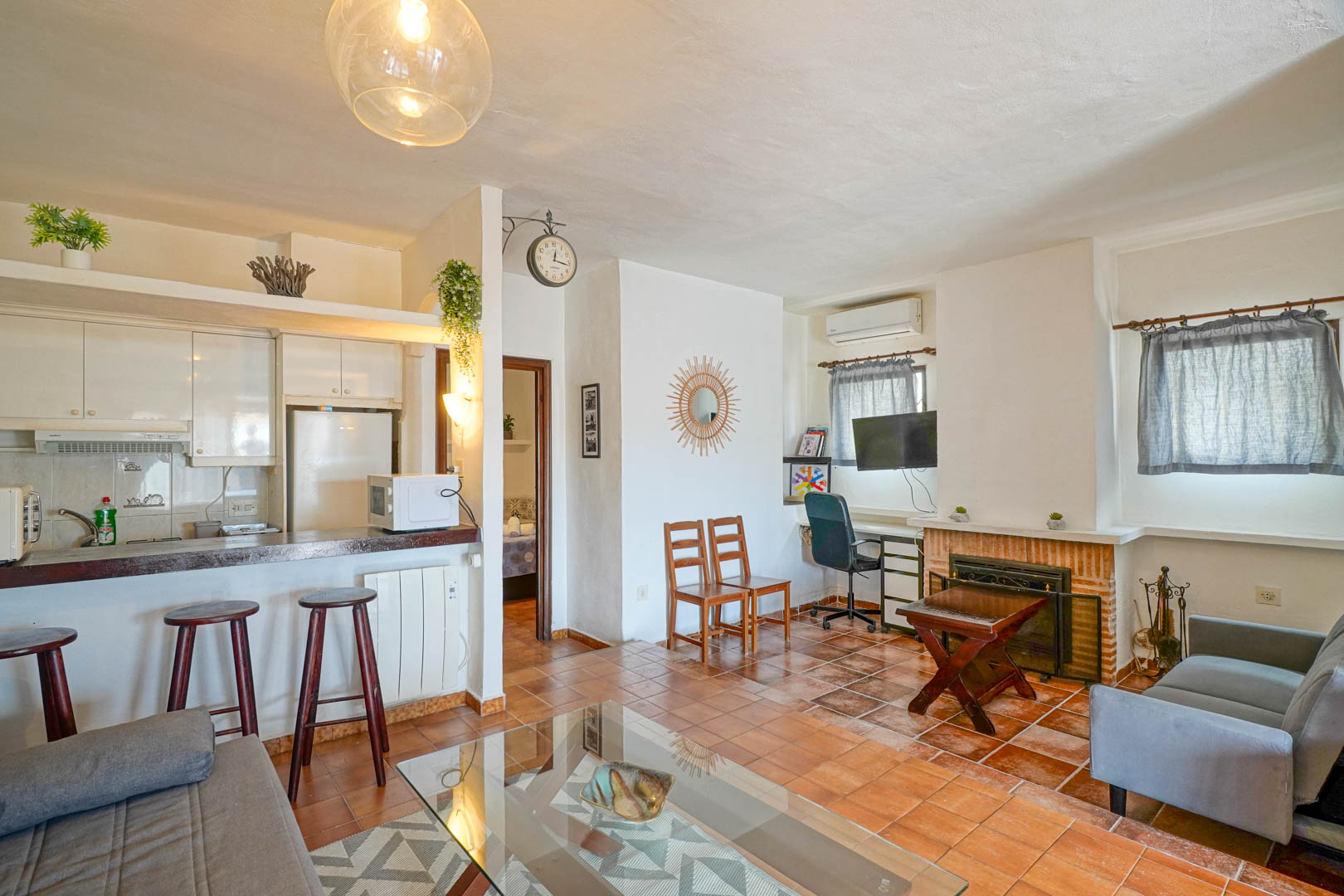 Open-plan living room featuring a brick fireplace, terracotta flooring, and a semi-integrated kitchen with a wooden breakfast bar.