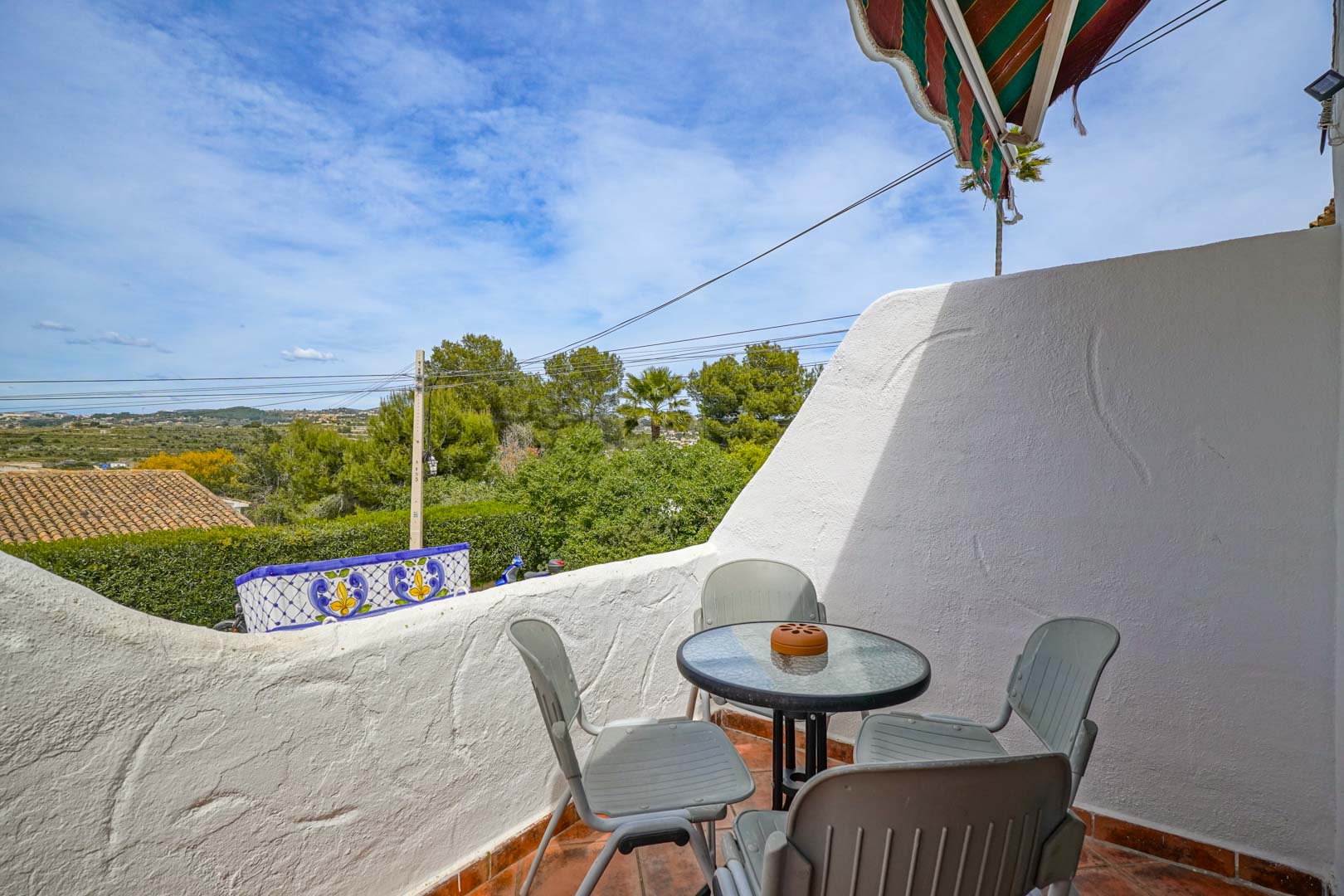 Outdoor terrace featuring terracotta flooring and a seating area, providing open views of the valley and Mediterranean greenery under a striped awning.