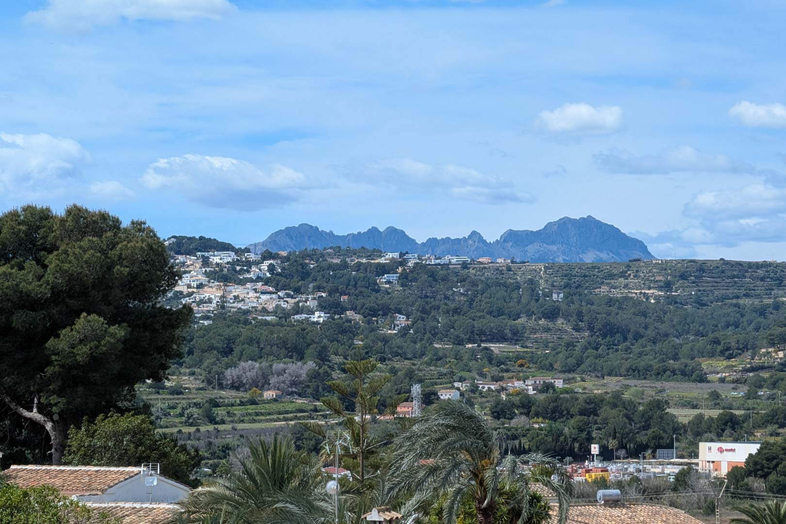 Panoramic views from the terrace overlooking the valley and mountains, featuring Mediterranean vegetation and the residential landscape of Moraira under a clear sky.