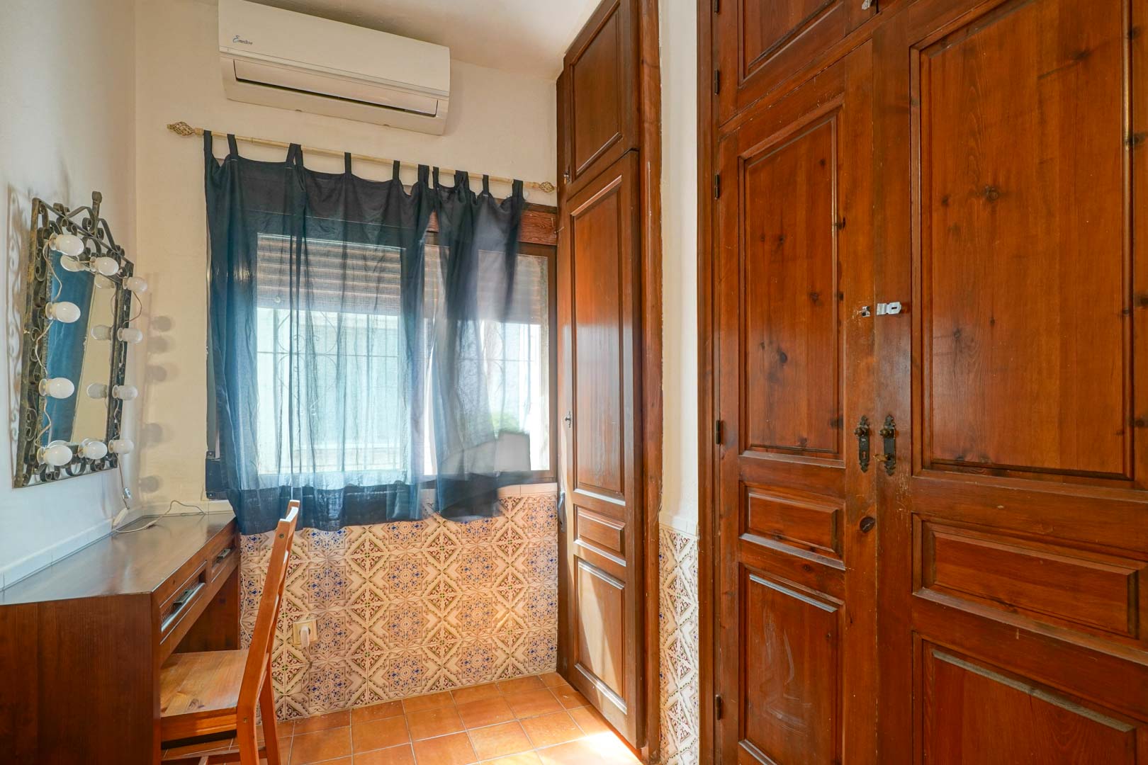 Vanity area featuring a wooden desk and illuminated mirror, positioned next to large dark wood built-in wardrobes and traditional patterned wall tiles.