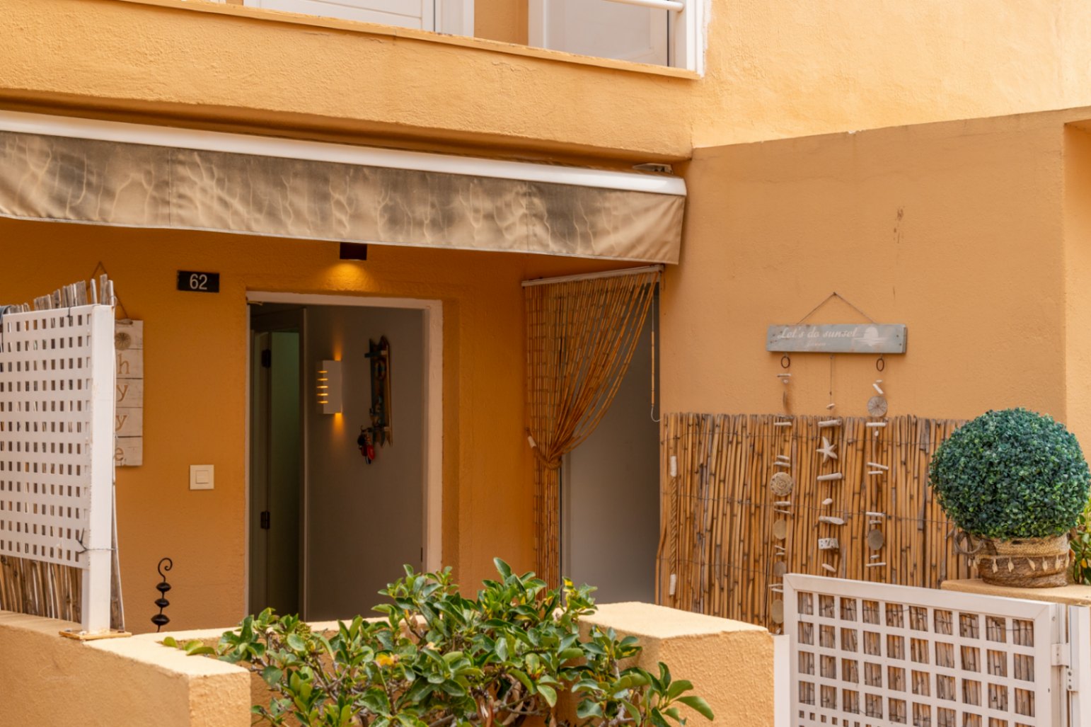 Ground floor entrance with awning, open doorway, and bohemian decor with beach elements.