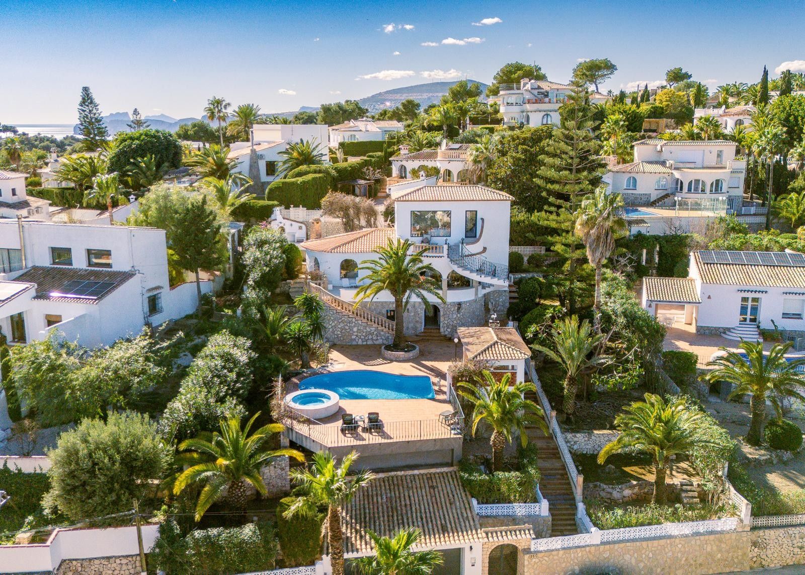 Aerial view of the multi-level villa featuring a private pool, circular jacuzzi, and sun terraces set within a landscaped Mediterranean garden with palm trees.