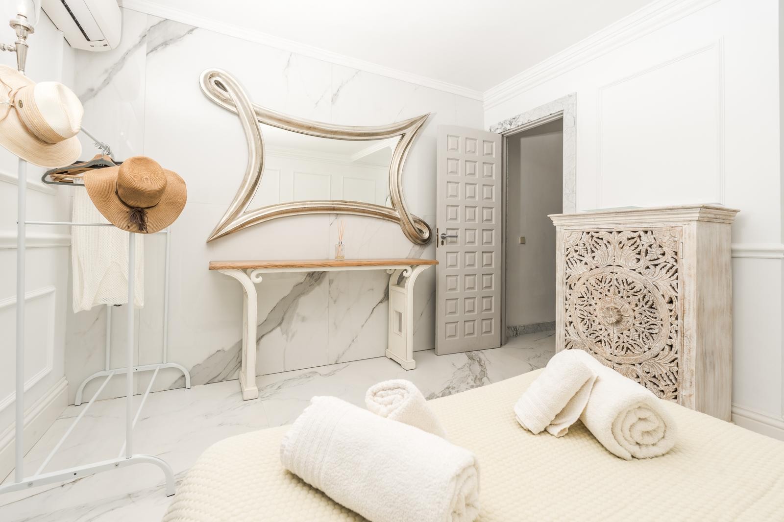 Bedroom featuring marble-clad walls and floors, an ornate silver-framed mirror, and a hand-carved decorative wooden chest.